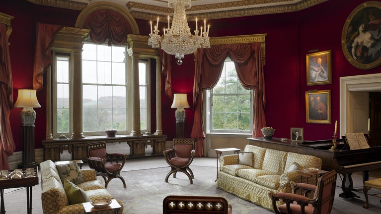 The Octagon Drawing Room at Basildon Park, Berkshire. The ornate frieze and heavy ceiling are in Italian 16th-century style but were designed by Papworth in 1840. The walls are covered with red felt, a popular colour in the 18th century. The large chandelier is Regency, and the mahogany armchairs in the Gothic style were designed by William Porden in 1810.